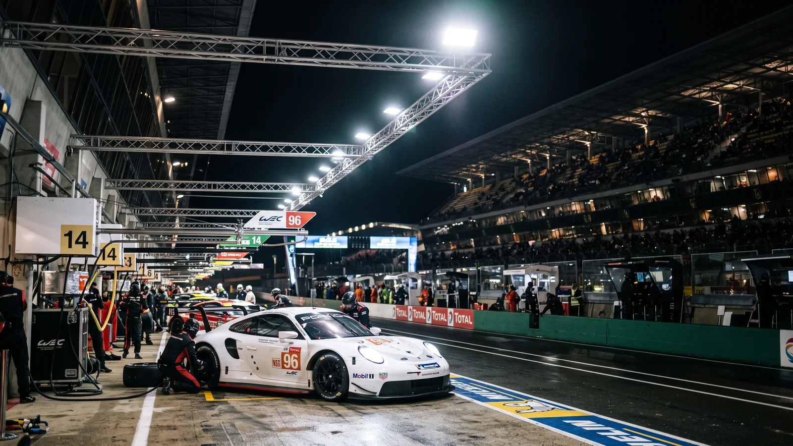 Race car being serviced in a floodlit pit lane at night